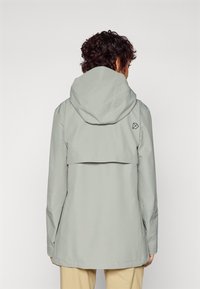 Veste imperméable gris clair avec capuche, présentant un design à dos superposé et un petit logo sur l'épaule gauche. Texture lisse et synthétique.
