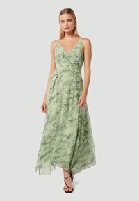 Robe maxi verte à motifs floraux avec décolleté en V, fines bretelles et silhouette fluide, présentant un détail noué au niveau du corsage et une texture douce.