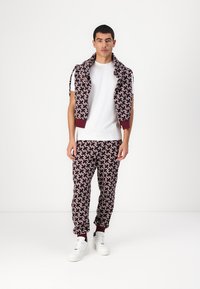 Pánský set volnočasového oblečení, který obsahuje vzorovaný burgundský svetr a odpovídající joggers, oba s pohodlným střihem a náplety. Bílé tenisky.