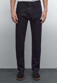 Mörka denimjeans med rak passform, fem fickor, subtil söm och en klassisk midja. Kombinerade med mörka mockaskor.