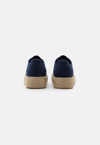 Scarpe in tessuto blu navy con dettagli perforati, caratterizzate da una suola in juta naturale testurizzata. Tacco arrotondato e apertura bassa.