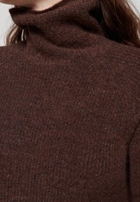 Maglione a collo alto lavorato a maglia marrone con una finitura morbida e testurizzata e un design aderente. Realizzato in un materiale caldo e morbido.