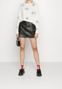 Maglione bianco con motivi a fiocco di neve, abbinato a una minigonna di pelle nera. Scarpe nere con calze rosse e beige. Piccola borsa in mano.