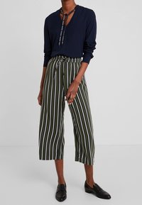 Marinblå blus med lång ärm och nyckelhålsringning samt knytning. Olivgröna högmidjade culottes med vita vertikala ränder. Svarta loafers.