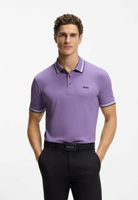 Polo viola con tessuto a trama, colletto a righe bianche e nere, e dettaglio con logo sul petto a sinistra abbinato a pantaloni neri.