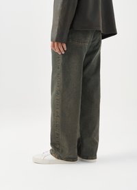 Φαρδιές, σκούρες πράσινες τζιν παντελόνες με ξεθωριασμένη υφή, με πλευρικές τσέπες και ίσια γραμμή, συνδυασμένες με λευκά αθλητικά παπούτσια.