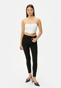 Top corto blanco sin tirantes con costuras estructuradas, combinado con pantalones negros ajustados y tacones negros puntiagudos, exhibiendo una silueta moderna y elegante.