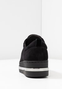 Černé semišové sneakerky s masivní černou podrážkou a kovovým stříbrným akcentem. Vyznačují se minimalistickým designem a zaobleným podpatkem.