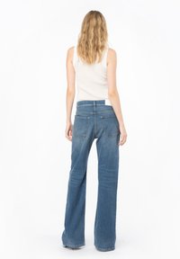 Jeans de tiro alto acampanados en denim azul medio, con cinco bolsillos, cierre de botón y un ligero lavado para textura y dimensión.