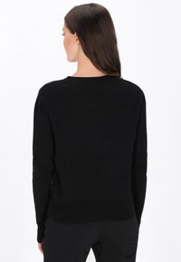 Svart ribbad tröja med långa ärmar och rund halsringning. Mjuk textur och åtsittande design, visad bakifrån, med en ren silhuett.