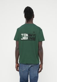 Πράσινο βαμβακερό μπλουζάκι με κοντά μανίκια, με μεγάλο ασπρόμαυρο λογότυπο "TOMMY JEANS" στην πλάτη. Casual εφαρμογή.