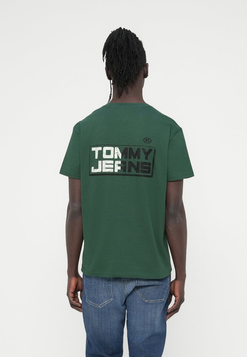 Πράσινο βαμβακερό μπλουζάκι με κοντά μανίκια, με μεγάλο ασπρόμαυρο λογότυπο "TOMMY JEANS" στην πλάτη. Casual εφαρμογή.
