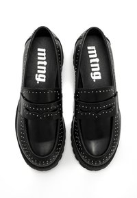 Une paire de mocassins en cuir noir avec des clous argentés autour des bords et de larges bandes sur le dessus, avec la marque "mtng" à l'intérieur des semelles.