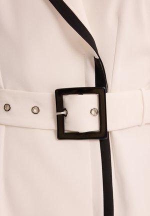 Biała tkanina z czarnymi wykończeniami, z szerokim paskiem z kwadratową czarną klamrą i srebrnymi elementami. Gładka tekstura i minimalistyczny design.