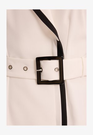 Biała tkanina z czarnymi wykończeniami, z szerokim paskiem z kwadratową czarną klamrą i srebrnymi elementami. Gładka tekstura i minimalistyczny design.