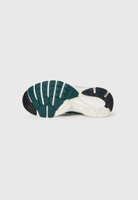 Shoe outsole featuring a multi-color design with a textured green, black, and white pattern; rugged tread for traction and stability.
