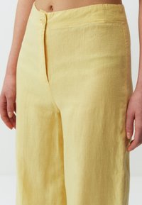 Geels linnen broek met een knoopsluiting, met een zachte textuur, wijde pijpen en een relaxed fit. De stof heeft een lichte, ademende kwaliteit.