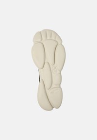 Semelle de chaussure avec un design texturé, présentant une couleur crème claire et des formes rondes irrégulières pour une meilleure adhérence et un amorti amélioré.