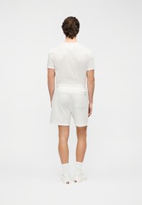 Σετ λευκό βαμβακερό μπλουζάκι και σορτς, άνετη εφαρμογή, λαιμόκοψη, ελαστική μέση, σορτς με πίσω τσέπη, συνδυασμένο με λευκές κάλτσες και αθλητικά παπούτσια.