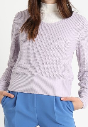 Maglione lavorato a maglia di un leggero lavanda con scollo rotondo e orlo a costine. Maniche lunghe e pattern testurizzato. Abbinato a pantaloni blu.