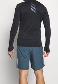 Czarna, długorękawowa koszulka sportowa z teksturowanej tkaniny i otworami na kciuki, w połączeniu z niebieskimi szortami z odblaskowymi akcentami i bocznymi kieszeniami.