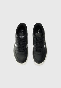 Sneakers neri Lacoste con striscia bianca, tomaia in pelle texturizzata, punta rotonda, lacci neri e logo sul lato. Suola in gomma.