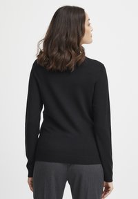 Maglione nero a maglia con maniche lunghe, scollatura rotonda e vestibilità slim. Texture liscia e dettaglio di orlo a coste. Vista dal retro.
