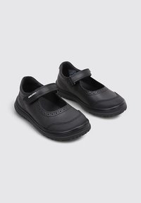 Zapatos escolares de estilo Mary Jane en negro con correas ajustables de gancho y bucle y suelas de goma duraderas y texturizadas, colocados uno al lado del otro sobre un fondo claro.