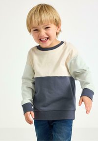 Bluza w blokach kolorystycznych w odcieniach jasnobeżowym, jasnej zieleni i granatowym. Miękka mieszanka bawełny z prążkowanymi mankietami i wykończeniem przy szyi.