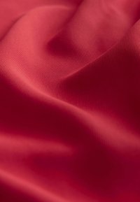 Röd texturerad tyg med en slät yta, som har subtil ribbing och mjuk drapering, vilket skapar milda vågor och veck i materialet.
