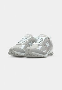 Gray athletic shoes with a mix of suede and mesh materials. Featuring a rounded toe, white accents, and rubber soles with textured detailing.