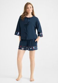 Granatowy zestaw odzieży dresowej z bawełny, składający się z bluzki z rękawami o długości trzy czwarte, dekoracyjnymi sznurkami oraz szortów z wzorem gwiazdy i księżyca na dolnej krawędzi.