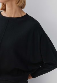 Schwarzer übergroßer Pullover mit weicher Textur, weiten Ärmeln und rundem Ausschnitt. Hat ein sauberes, minimalistisches Design und keine sichtbaren Muster.