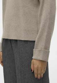 Beige Strickpullover mit gerippten Bündchen, kombiniert mit grauen strukturierten Hosen. Verfügt über einen leicht verkürzten Saum und einen weichen Stoff.