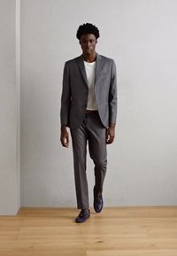 Costum gri cu un singur nasture, asortat cu o cămașă albă și pantofi albaștri. Materialul are o textură netedă, cu o croială modernă și linii clare.