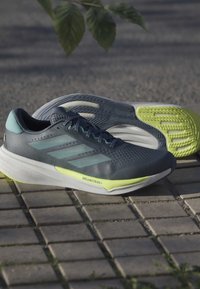 Scarpe da corsa da uomo con una parte superiore in mesh grigio scuro, dettagli blu chiaro e una suola giallo brillante. Presentano una suola testurizzata per una migliore aderenza.