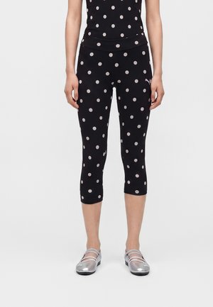 Kvinde iført sorte korte leggings og top med hvide prikker, kombineret med skinnende sølvfarvede flade sko med stropper.