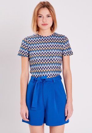 Haut à manches courtes à motifs zigzag bleus avec encolure ronde, associé à un short bleu taille haute avec une ceinture en tissu à la taille.