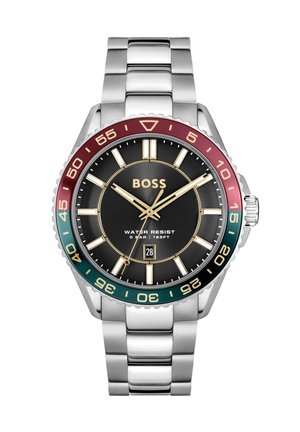 Silberne Metallarmbanduhr mit schwarzem Zifferblatt, goldenen Akzenten, rotem und grünem Lünettenring, Datumsanzeige bei sechs Uhr und Wasserdichtigkeitskennzeichnung.