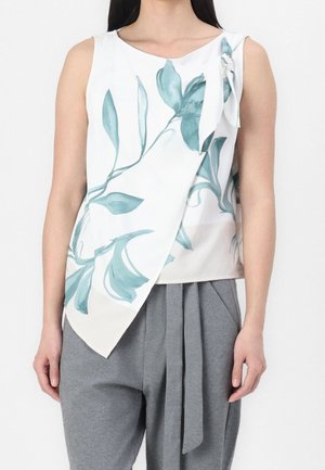 Biała top bez rękawów z niebiesko-zielonym nadrukiem liści, asymetryczną przednią klapą i kokardą na ramieniu, zestawiona z szarymi plisowanymi spodniami.