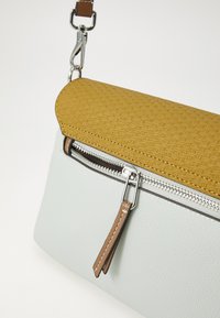 Sānu soma ar teksturētu dzeltenu augšpusi, gludu gaiši pelēku ķermeni, sudraba rāvējslēdzi un brūniem ādas akcentiem.