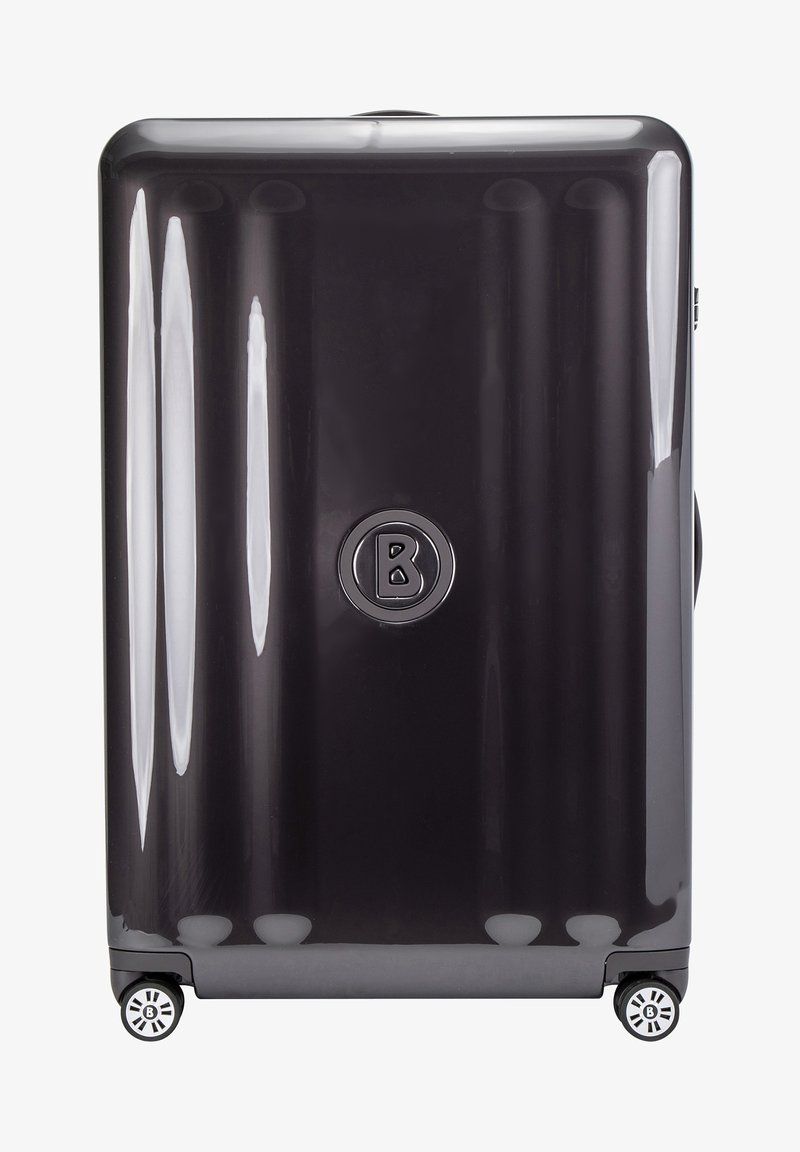 Kovakova matkalaukku kiiltävän tummanharmaan värinen, jossa on pystysuorat urat, ympyrälogo keskellä ja neljä monisuuntaista pyörää pohjassa.