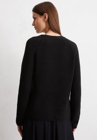 Schwarzer gestrickter Pullover mit geribbelter Textur, Raglanärmeln und einem einfachen Rundhalsausschnitt. Der Stoff wirkt dick und warm.