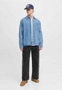 Lichtblauwe denimjack met knopen, borstzak, lange mouwen, gecombineerd met zwarte wijde broek en bruine instappers. Marineblauwe pet met logo.