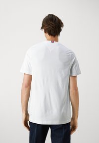 Tricou alb din bumbac cu mâneci scurte, având o mică dungă colorată pe spatele gâtului și o margine dreaptă.