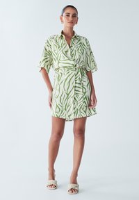 Kortærmet kjole med krave i sart grønt stof med et bladmønster. Har et bånd i taljen og en lige snit, der går over knæet.