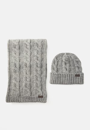 Écharpe et bonnet en tricot gris avec des motifs en câble, tous deux présentant des bords côtelés et de petites étiquettes de marque sur un fond blanc.