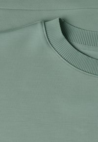 Gros plan d'un pull vert clair à col rond montrant un col côtelé et une texture de tissu tricoté lisse.
