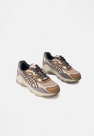 Baskets de sport dans des tons marron et beige, dotées de matériaux en mesh et en daim, avec une semelle épaisse, un design à lacets et des accents noirs sur le talon.