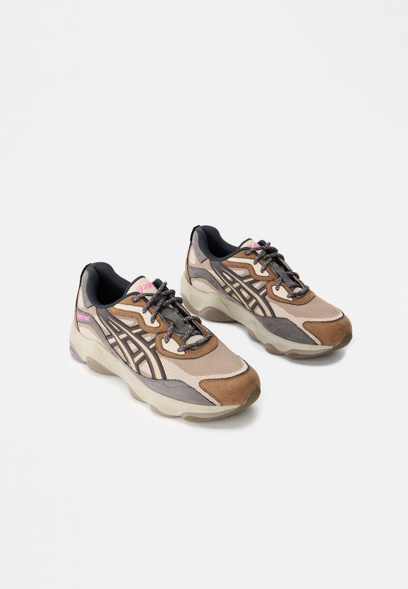 Athletic shoes in brown and beige tones, featuring mesh and suede materials, a chunky sole, lace-up design, and black accents on the heel.